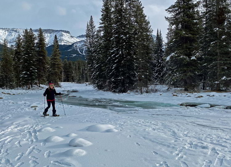An image of a woman snowshoeing along Baker Creek in Banff National Park, Alberta, Canada. 
