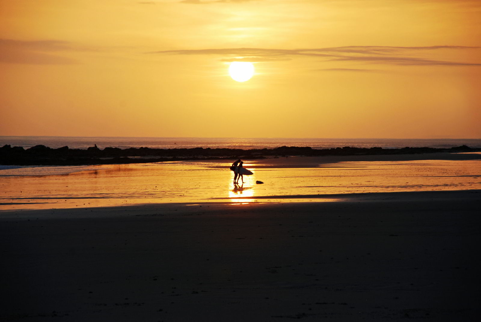 An image of two surfers carrying their surfboards at Playa Hermosa Beach at sunset - surfing in Costa Rica