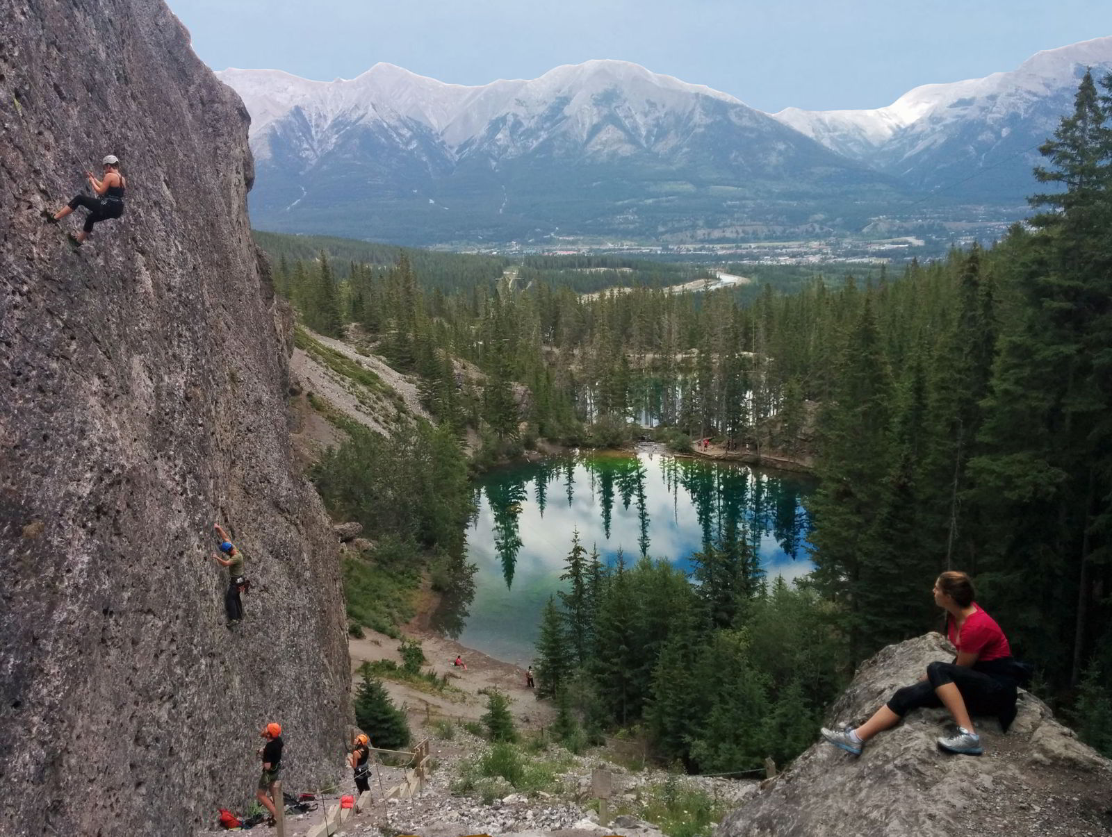 An image of a young woman watching rock climbers scaling a cliff above the Grassi Lakes in Canmore, Alberta - Grassi Lakes hike.