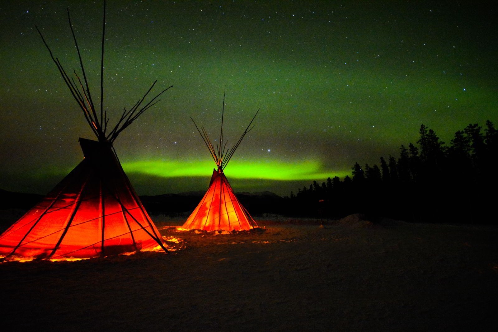 An image of the Yukon northern lights in winter with two tipis in the foreground.