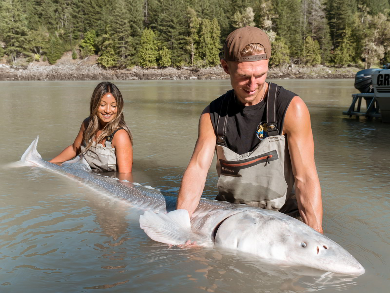 An image of a couple holding a sturgeon in a river.