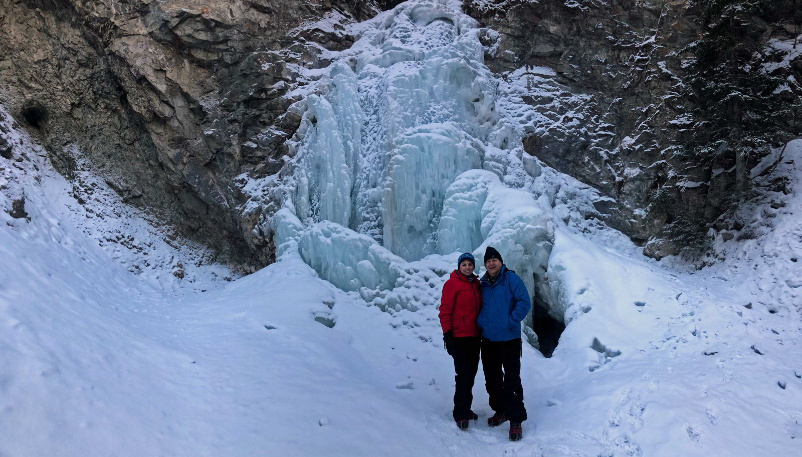 An image of a couple standing in front of the frozen Star Creek Falls in Crowsnest Pass, Alberta, Canada.