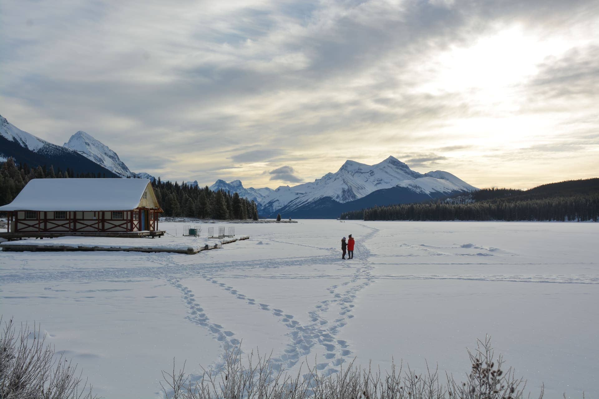 Two people standing on snow covered lake with mountains in background