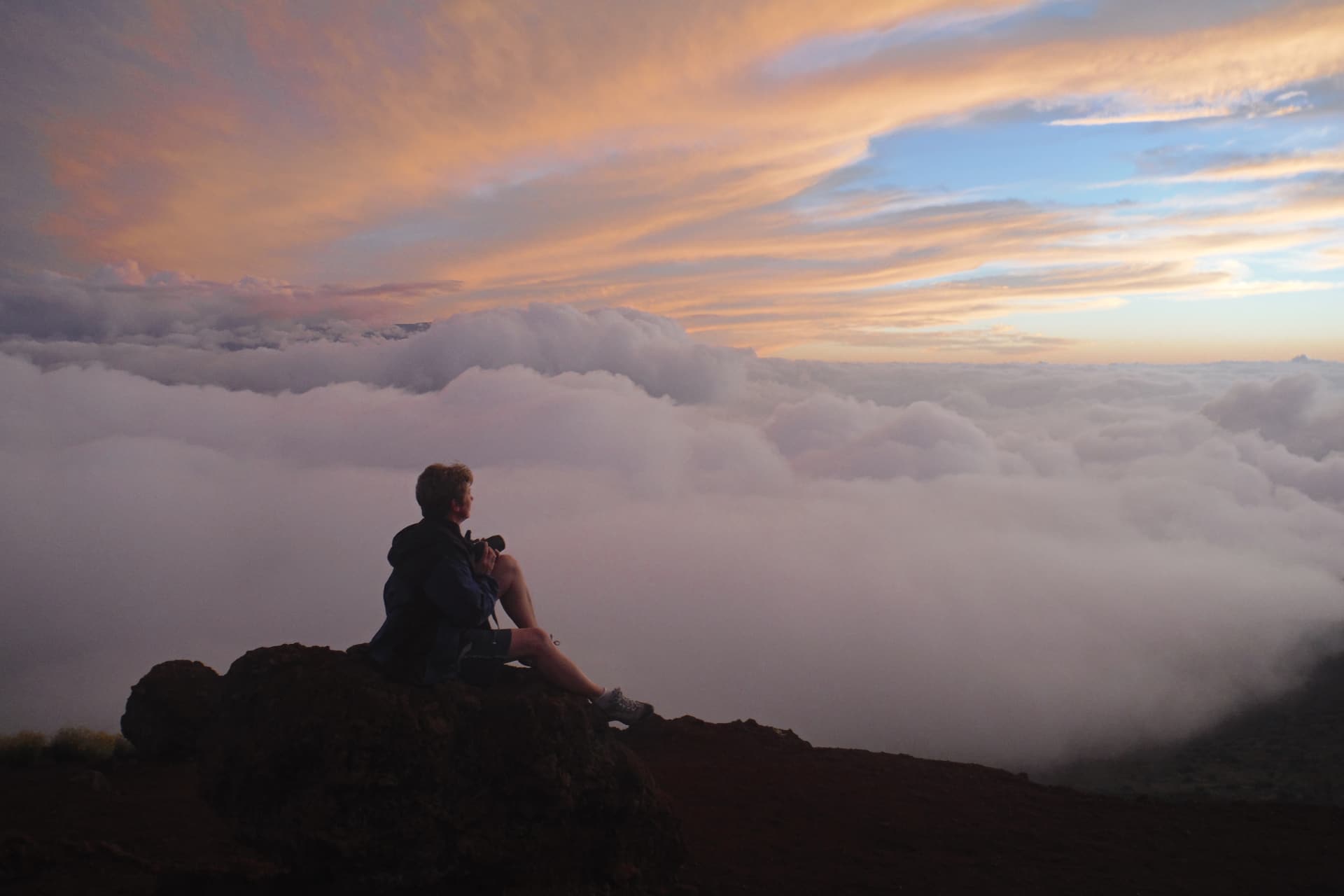 Woman sitting on rock with camera in hand and clouds in background