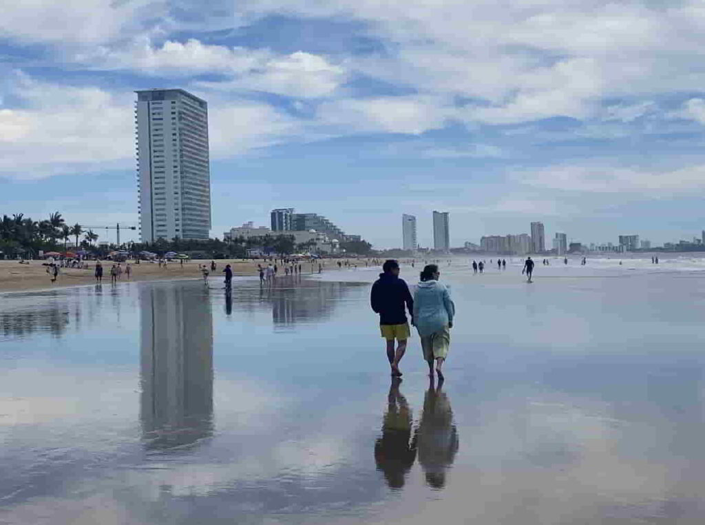 An image of two people walking on the beach in the Golden Zone in Mazatlan, Mexico. 